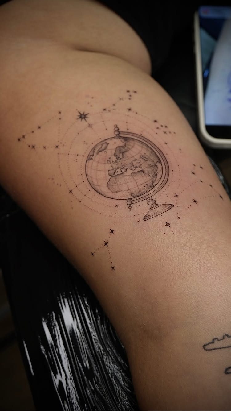 Globe tattoo surrounded by stars and constellation lines on a person's skin