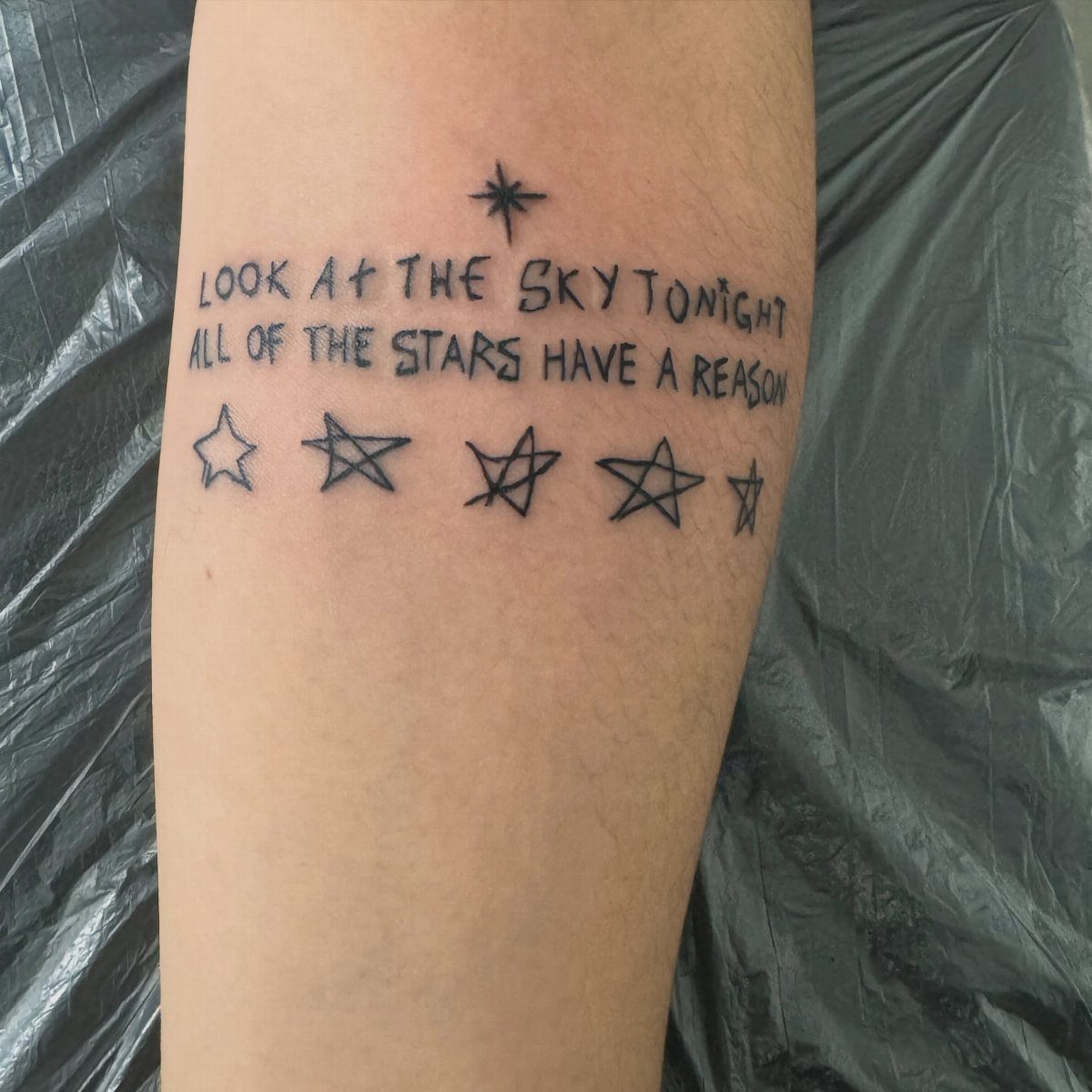 Tattoo on an arm with song lyrics and small stars in black ink.