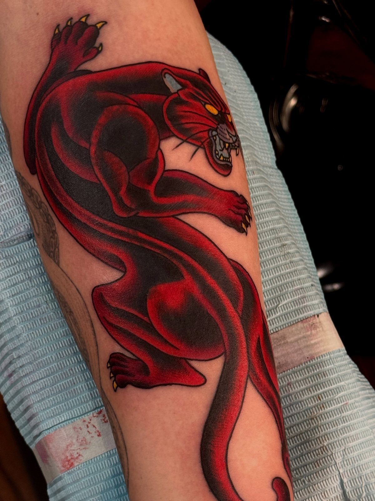 Red and black panther tattoo covering an older tattoo on a person's arm.