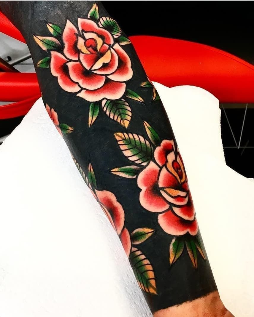 Blackout tattoo on an arm with red roses and green leaves integrated throughout.