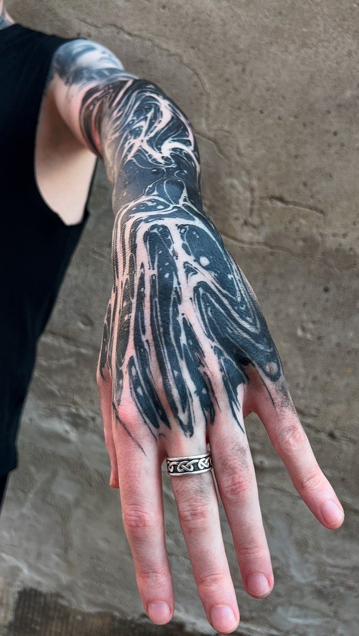 Abstract black ink tattoo with flowing swirls covering a person's arm and hand.