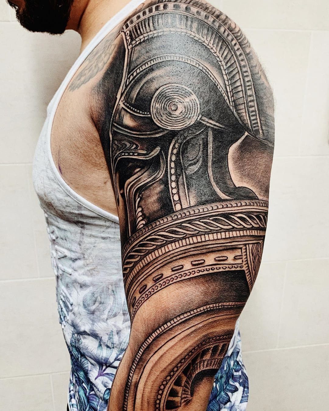 Biomechanical helmet tattoo in black and grey ink covering a person's upper arm.