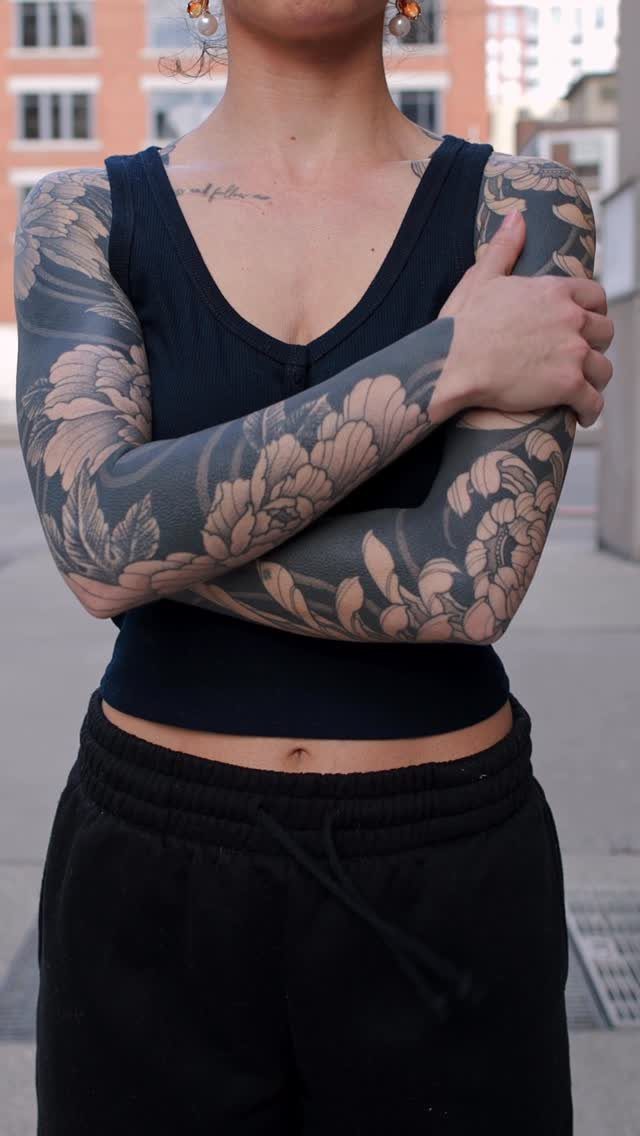 Full arm sleeve tattoo with large black and grey floral designs on a person.