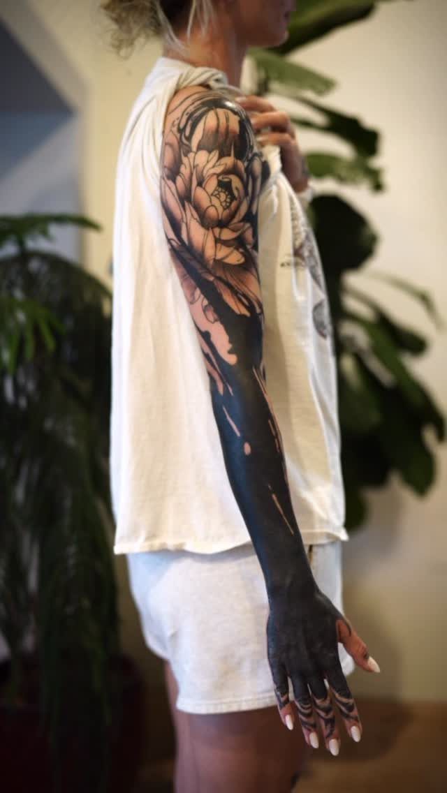 Arm tattoo with floral shoulder design and solid black ink covering the forearm.