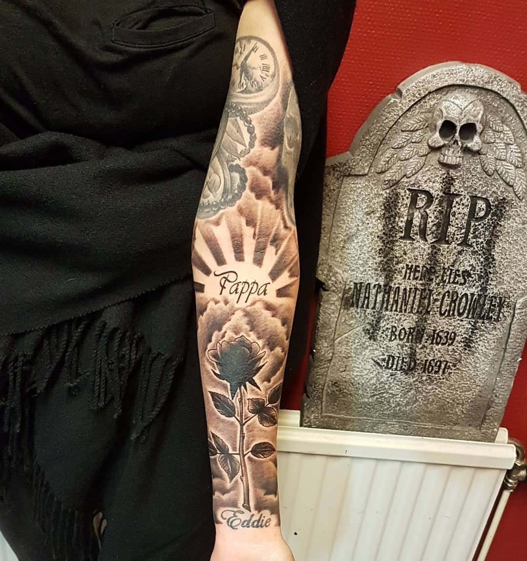 Arm sleeve tattoo with a clock and rose next to a decorative tombstone.