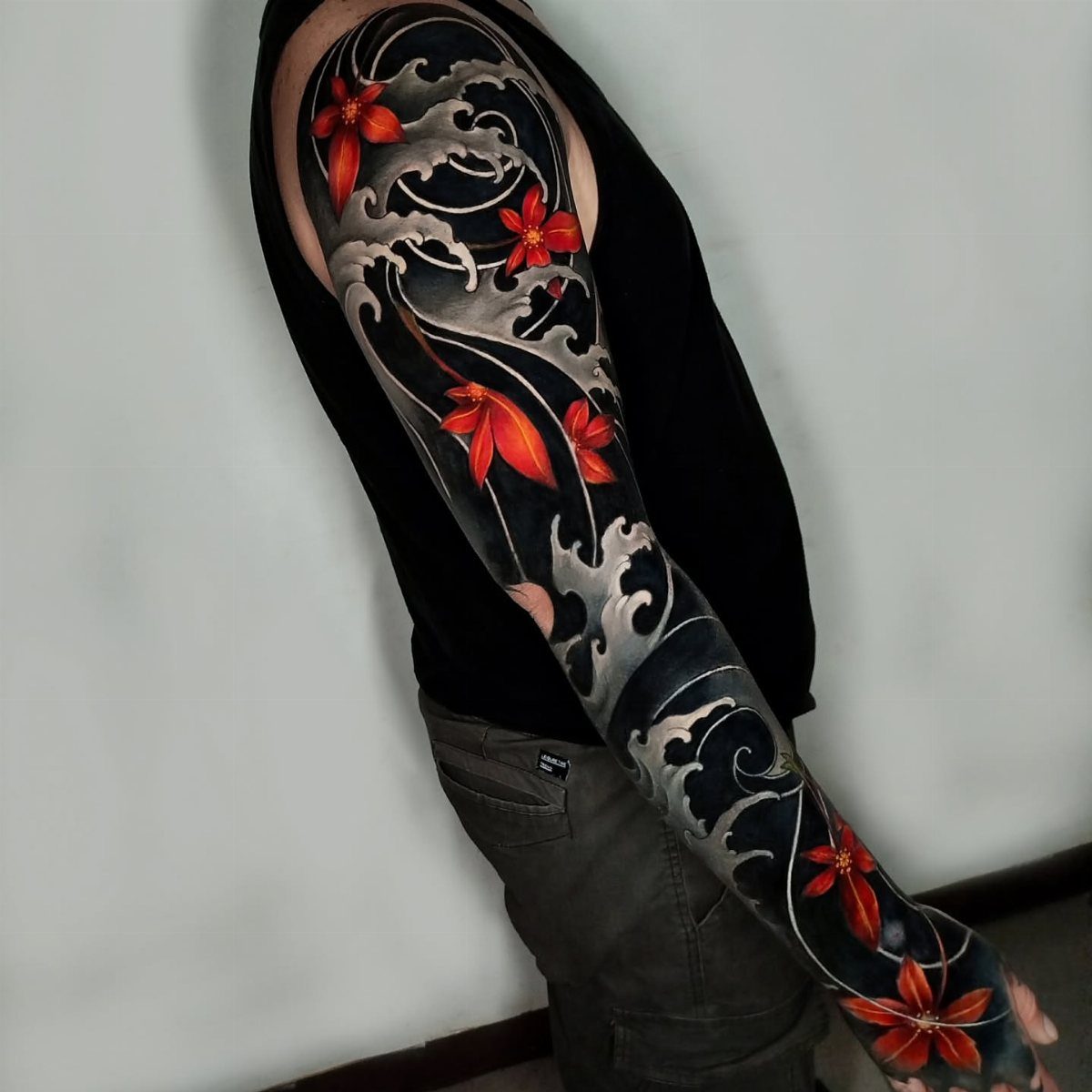 Full sleeve tattoo with black swirling waves and red flowers on a person's arm.