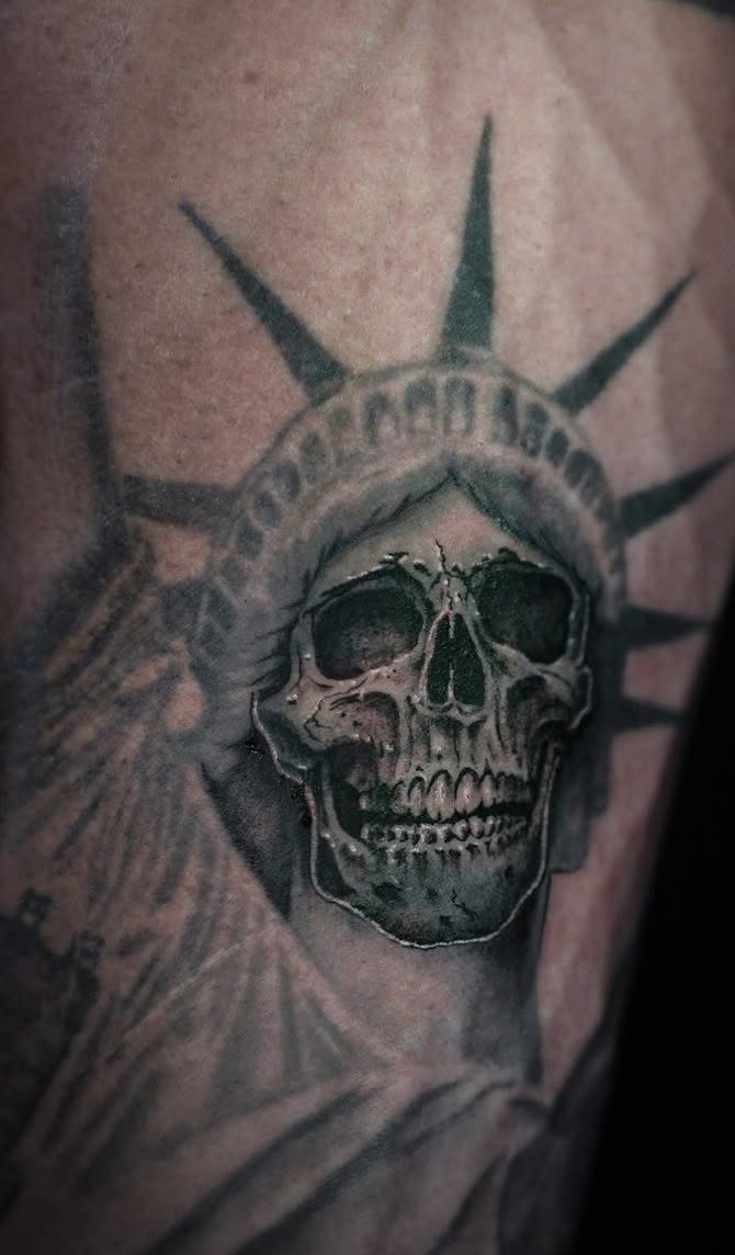 Skull tattoo wearing the Statue of Liberty's crown on a person's arm.