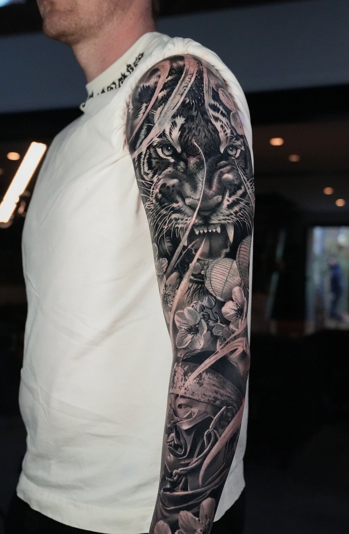 Detailed black and grey tattoo sleeve featuring a tiger on a person's arm.