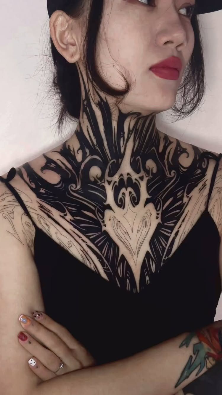 Woman with a large, symmetrical black ink tattoo covering her neck and chest.