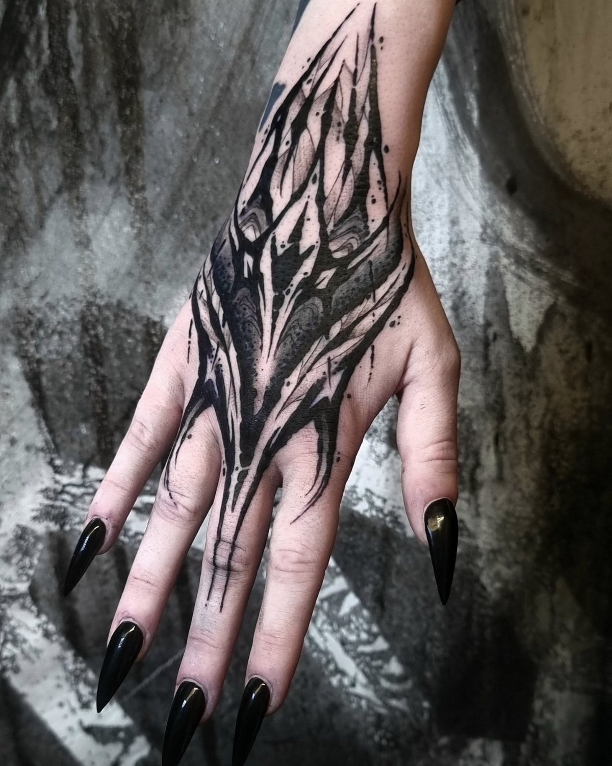 Hand with a bold black ink tattoo and long pointed black nails.