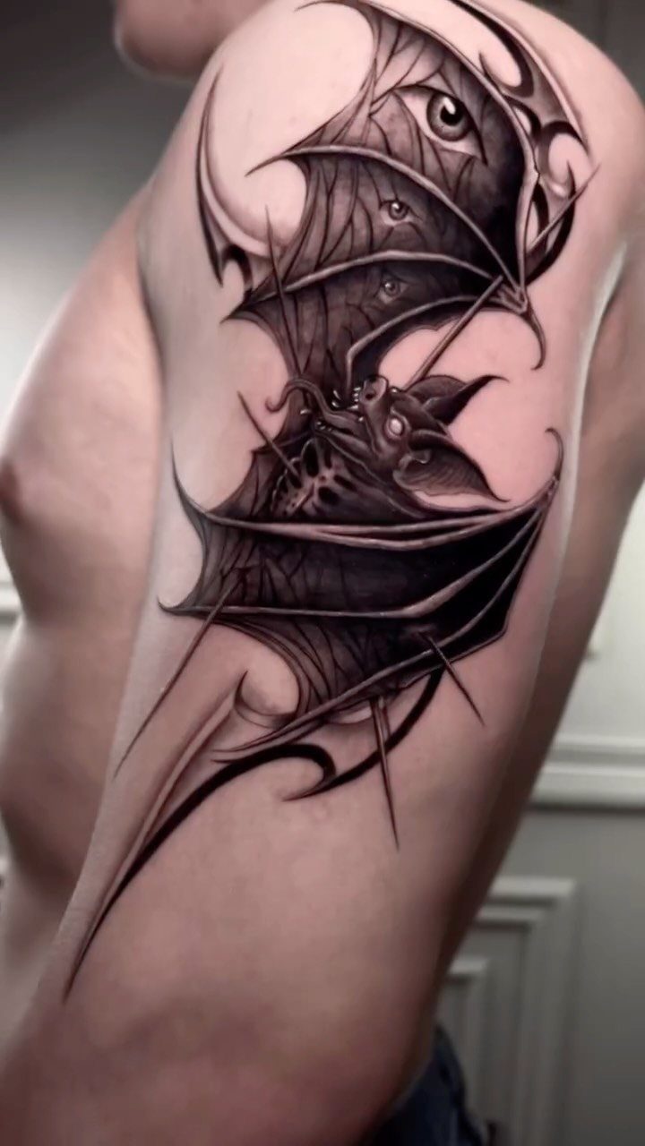 Bat tattoo with detailed wings and an eye on a person's upper arm.