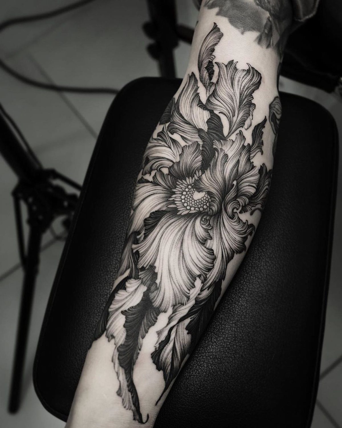 Detailed black ink floral tattoo on a person's forearm resting on black leather.