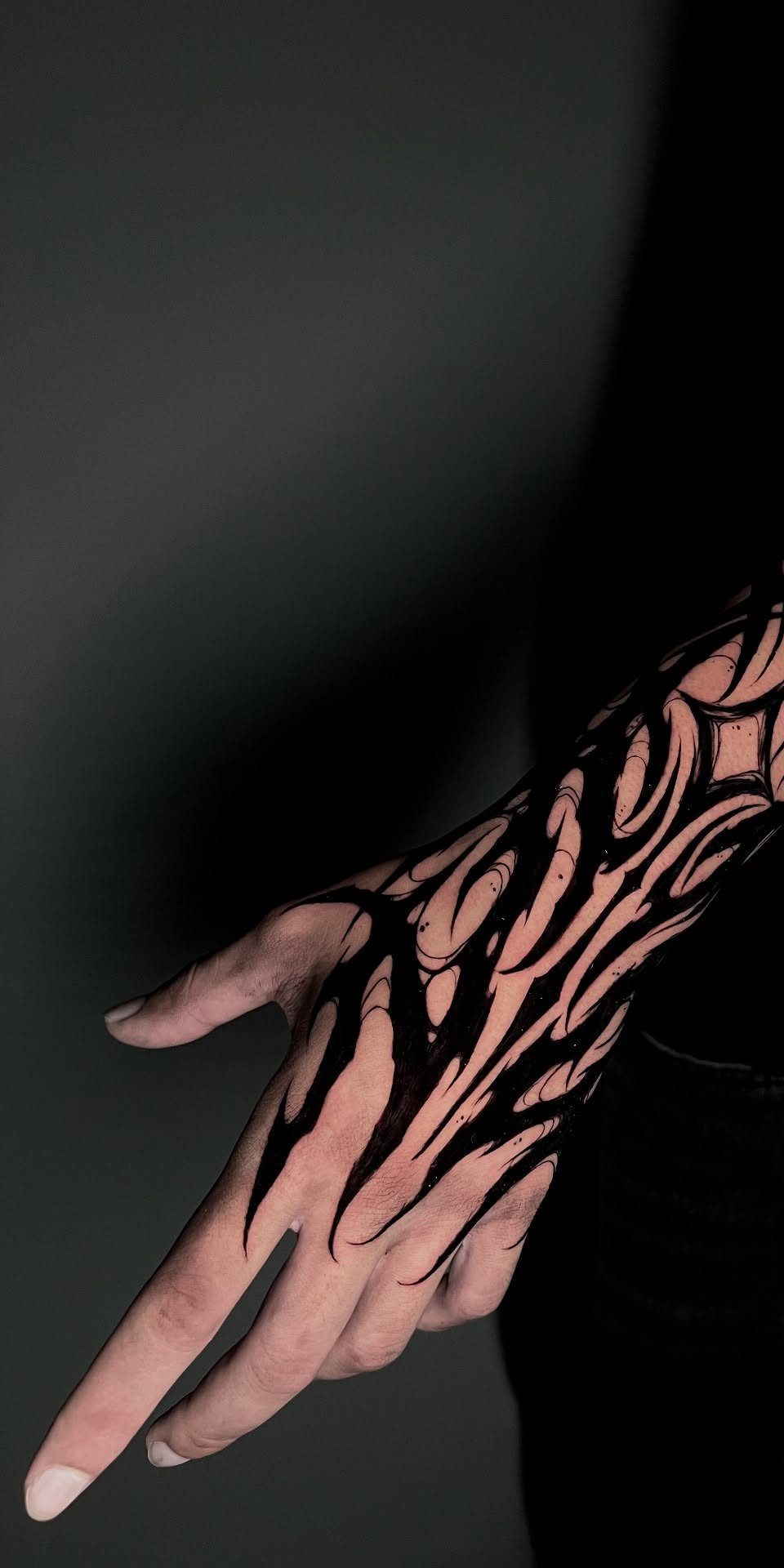Hand and forearm with bold black ink organic flowing tattoos on dark background