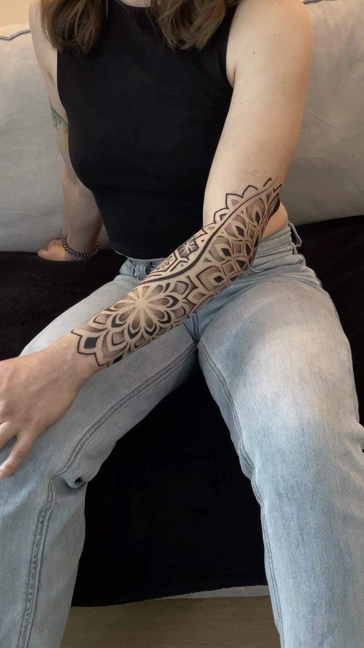 Forearm tattoo with a black ink mandala and geometric patterns on a person