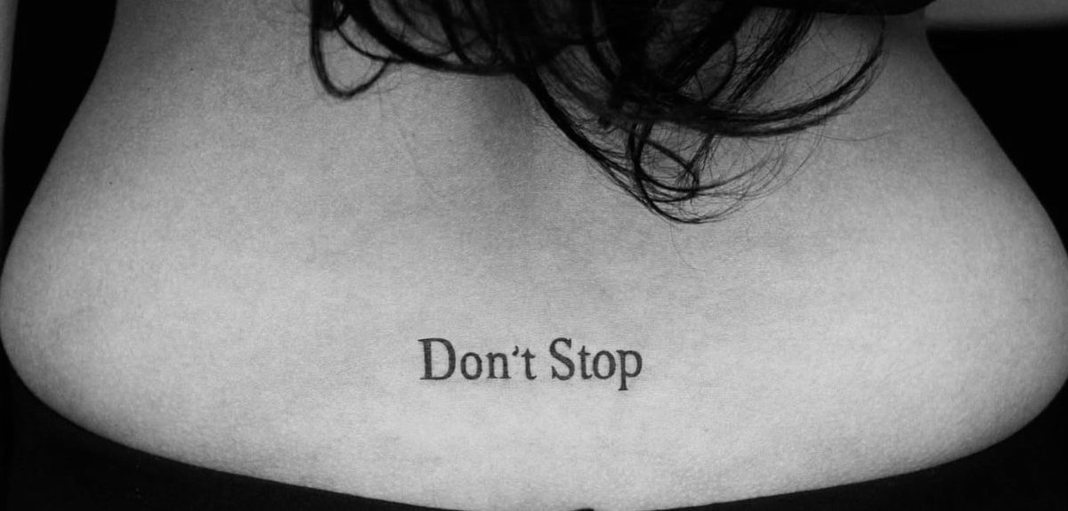 Small text tattoo reading Don't Stop on a person's upper back.