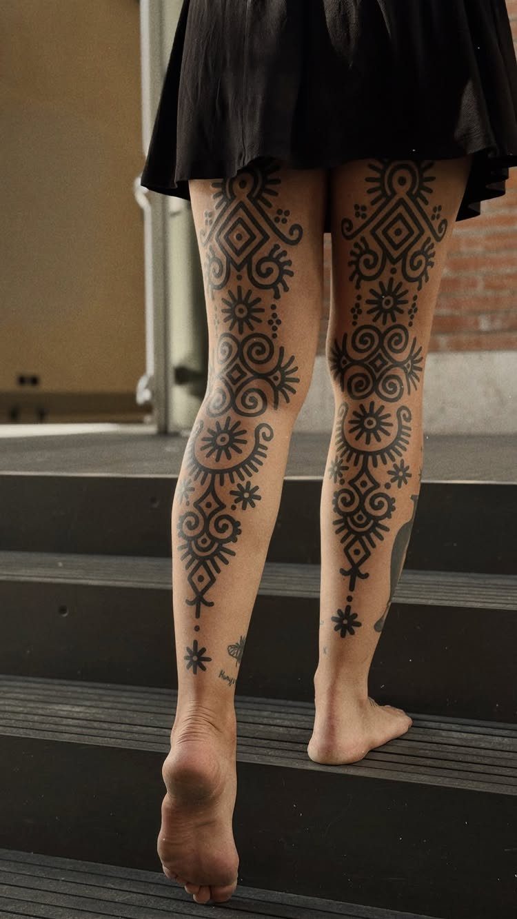 Legs with symmetrical geometric black ink tribal tattoos standing on dark stairs