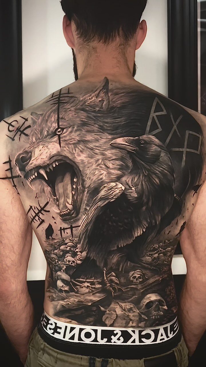 Large black and grey tattoo of a wolf and raven on a man's back.