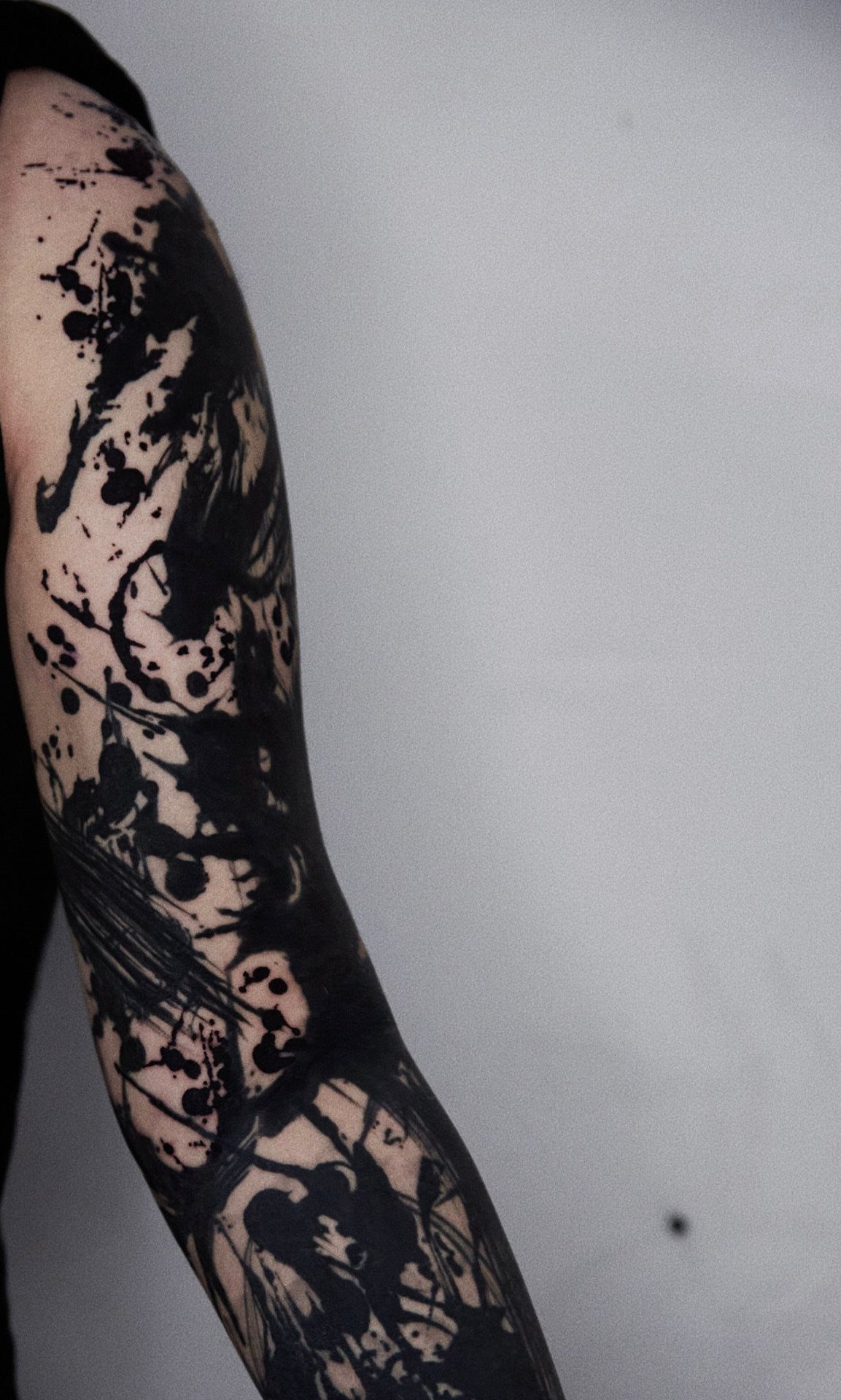 Arm with a black ink splatter tattoo featuring abstract blots and drips.