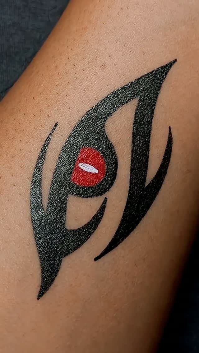 Stylized eye tattoo with black curved lines and a red iris on skin.