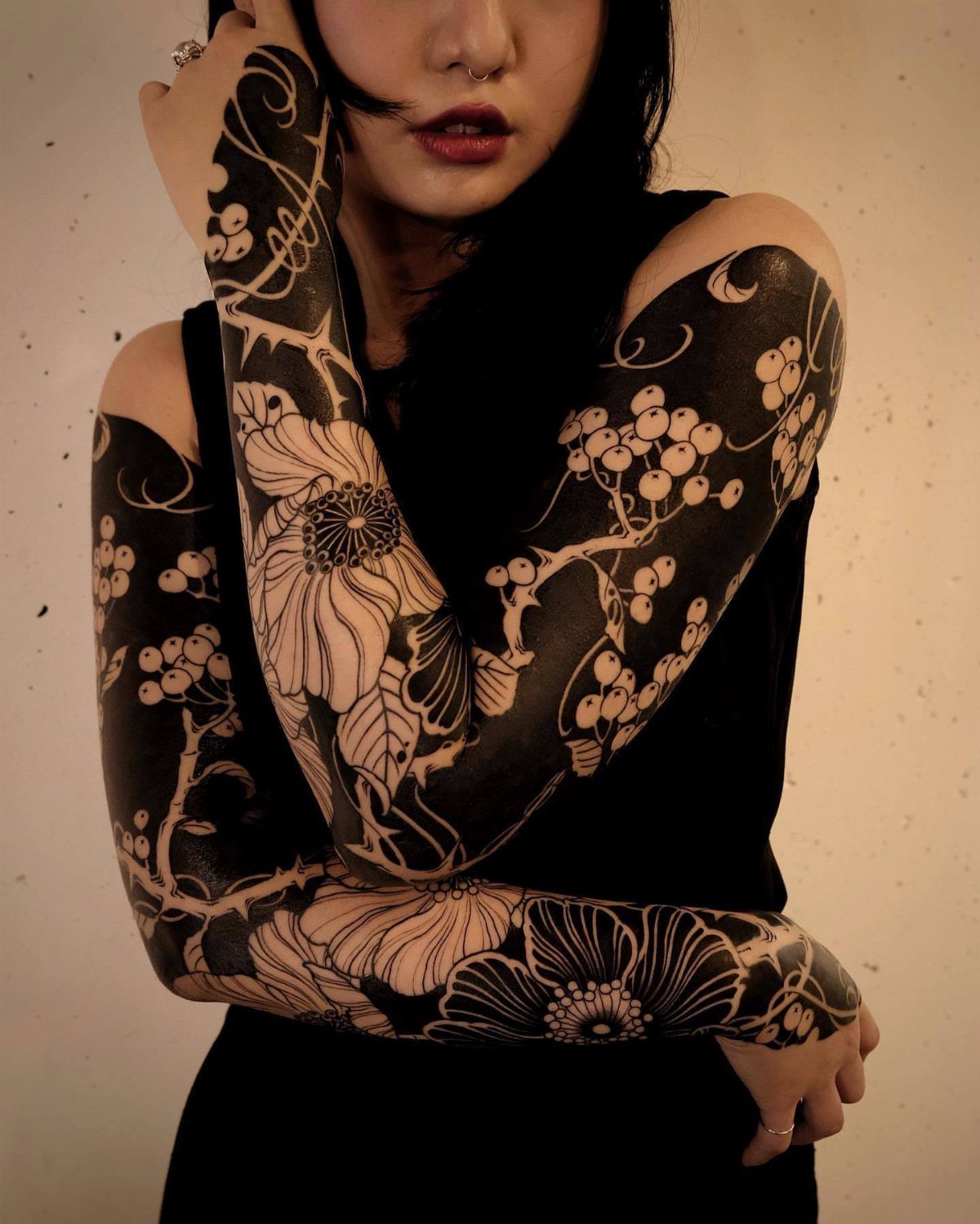 Floral black ink tattoos covering the arms of a person wearing black clothing.