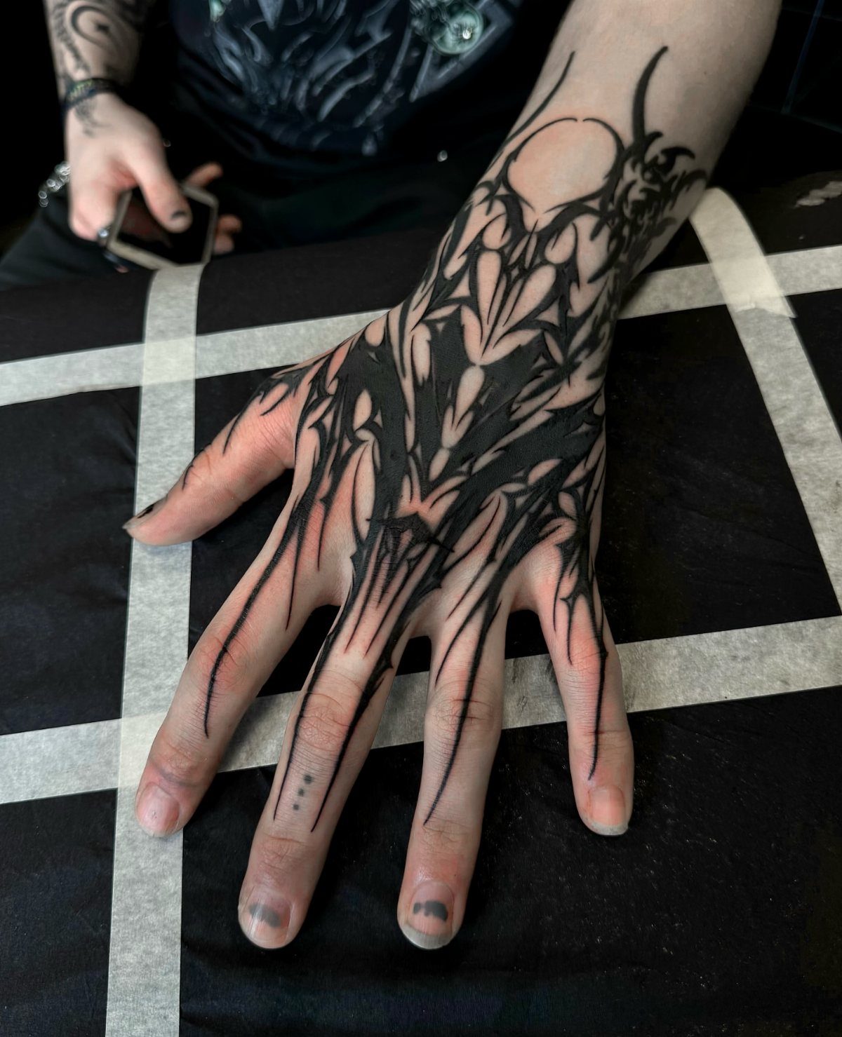 Hand and wrist with a detailed black ink biomechanical tattoo on a black surface.