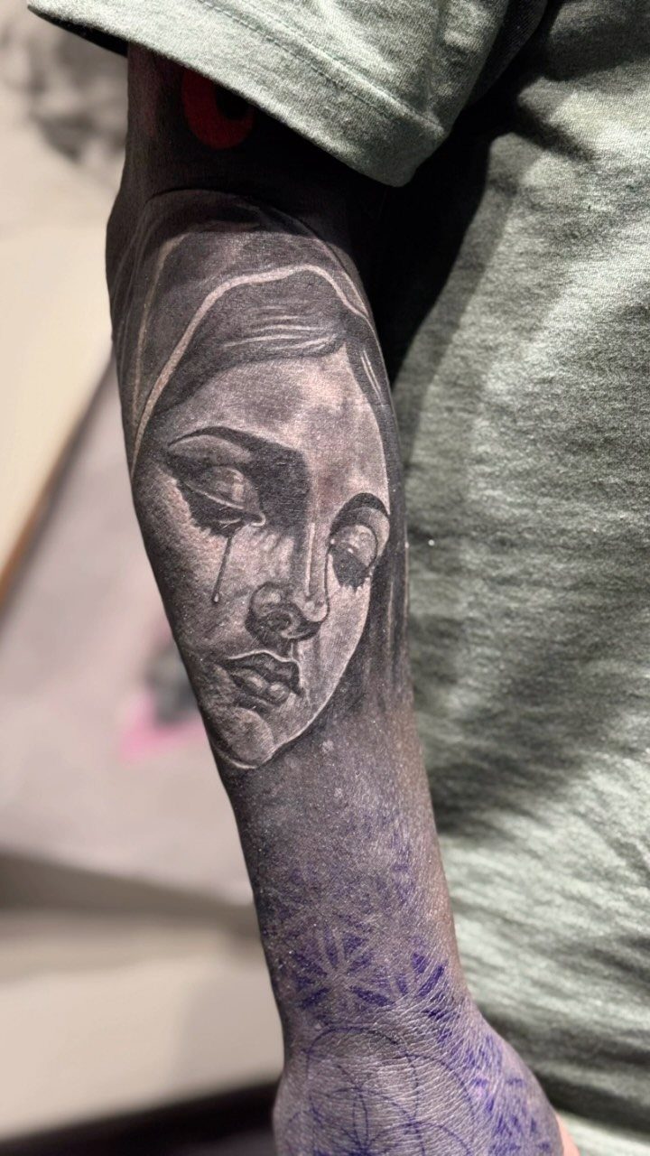 Tattooed arm showing a woman's face surrounded by solid black ink and patterns.