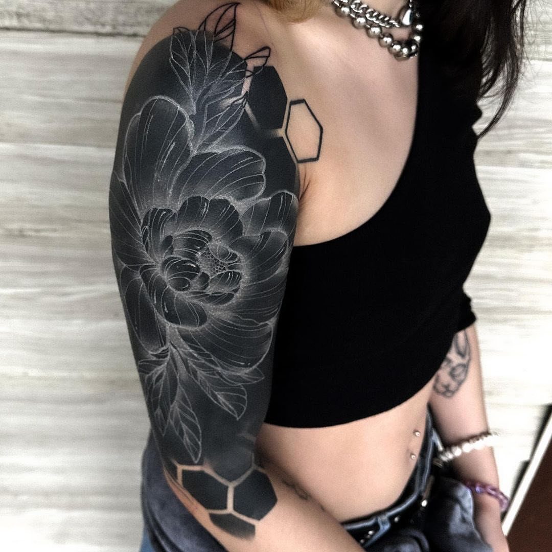 Blackout sleeve tattoo with white ink floral and geometric designs on an arm.