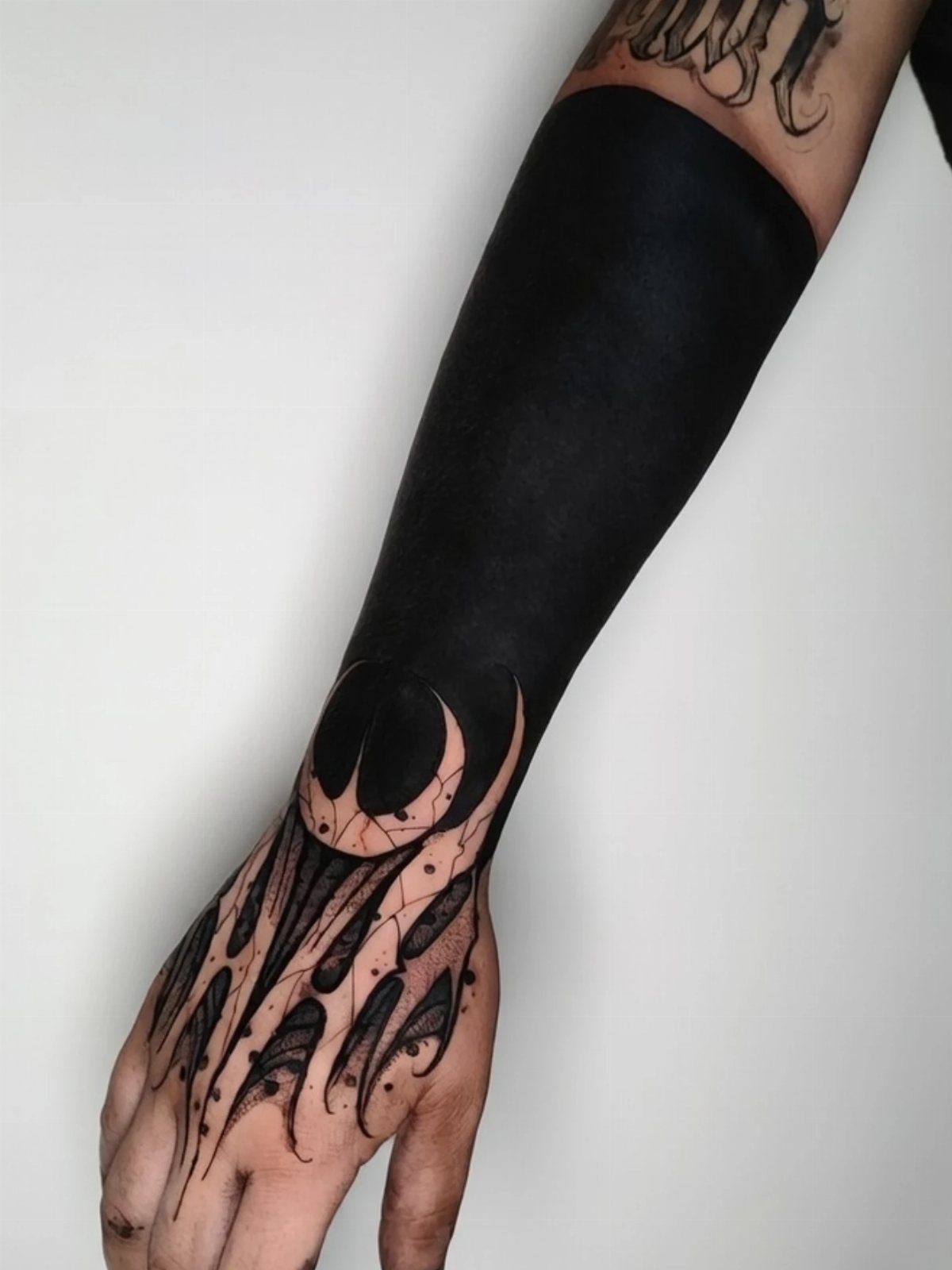Blacked out tattoo on forearm transitioning into claw designs on the hand.