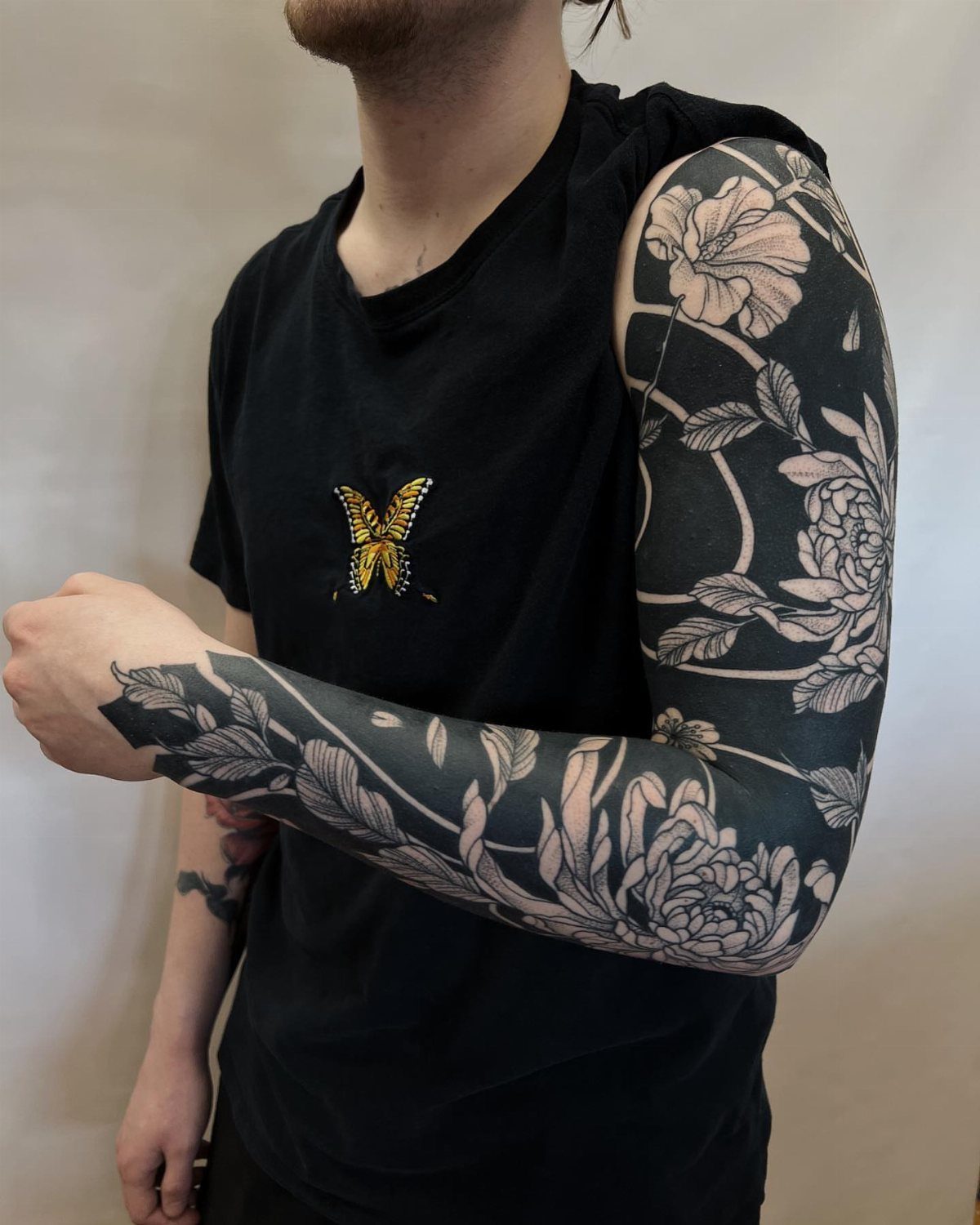 Full arm blackout tattoo with intricate white floral patterns and leaves on a person.