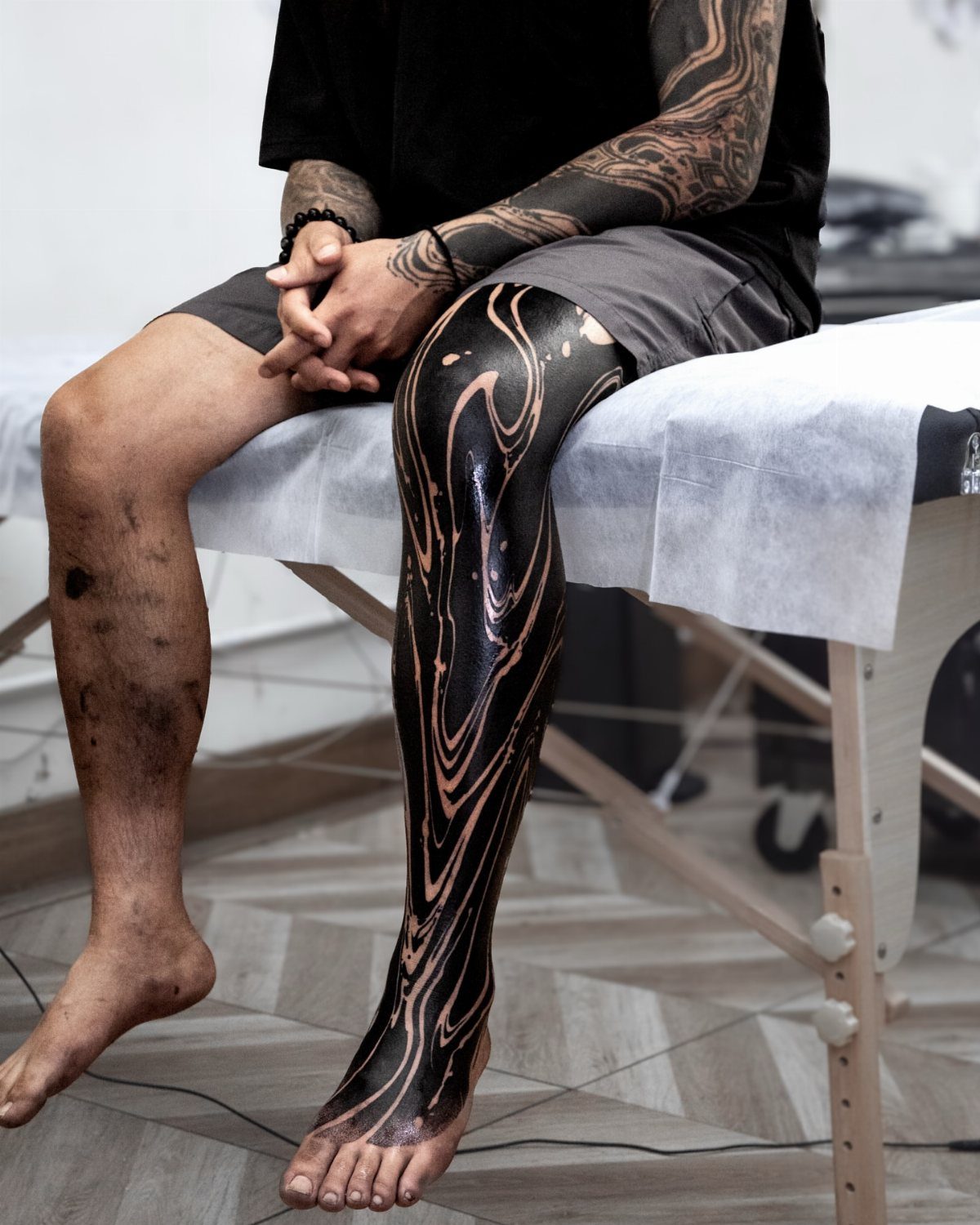 Leg covered in a glossy black ink tattoo with swirling organic patterns.