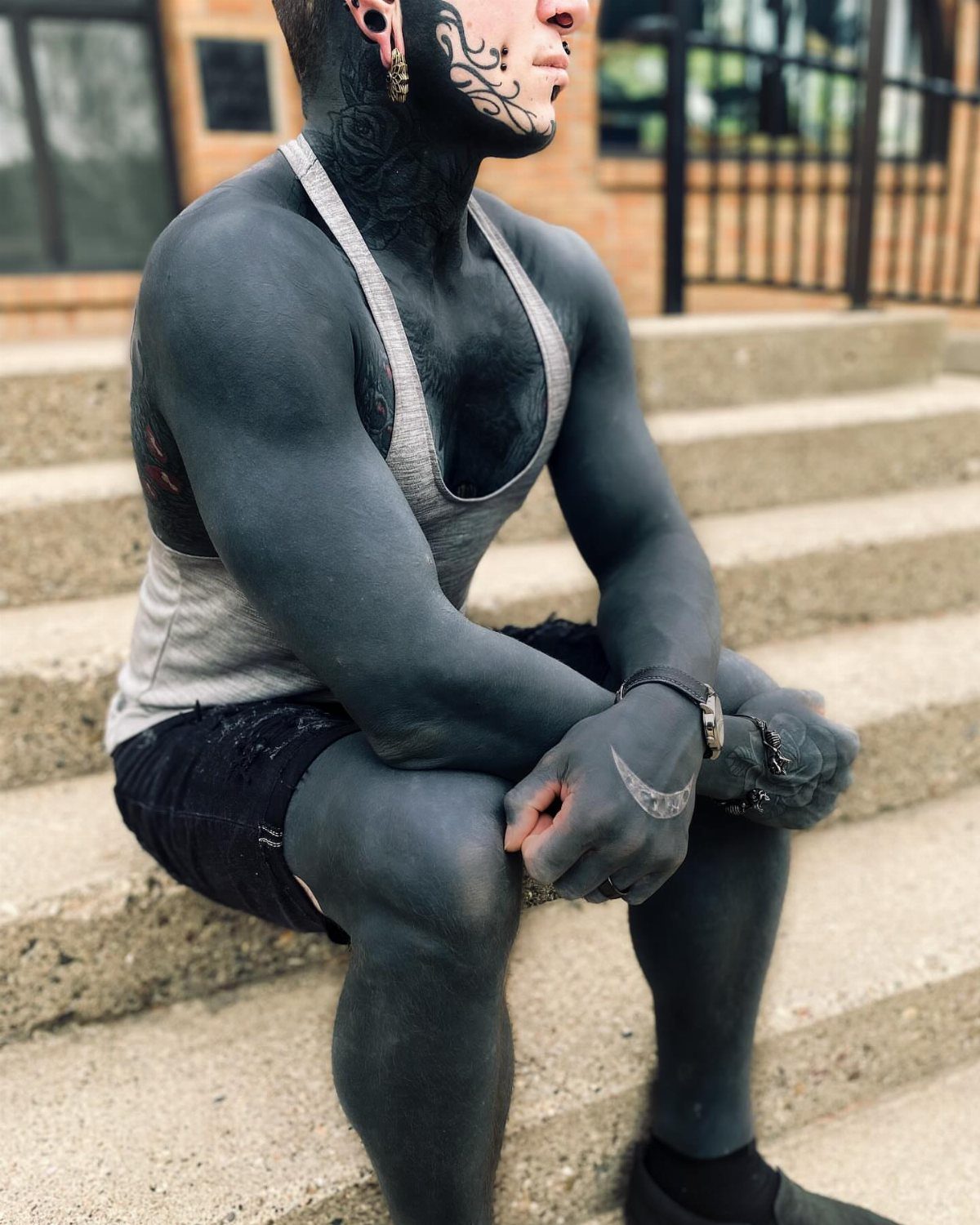 Man with extensive solid black ink tattoos covering his neck, arms, and legs.