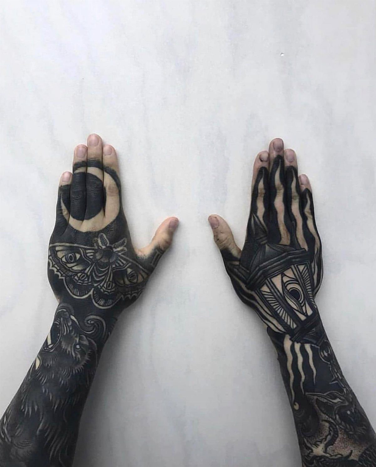 Tattooed hands and forearms with heavy blackout ink and intricate geometric patterns.