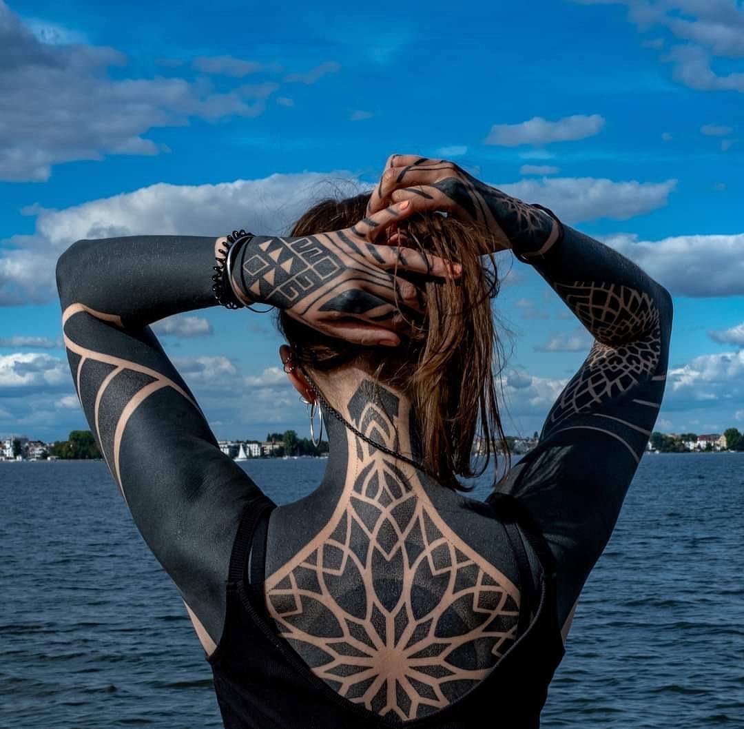 Person with blacked out tattoos featuring a large negative space mandala on their back.