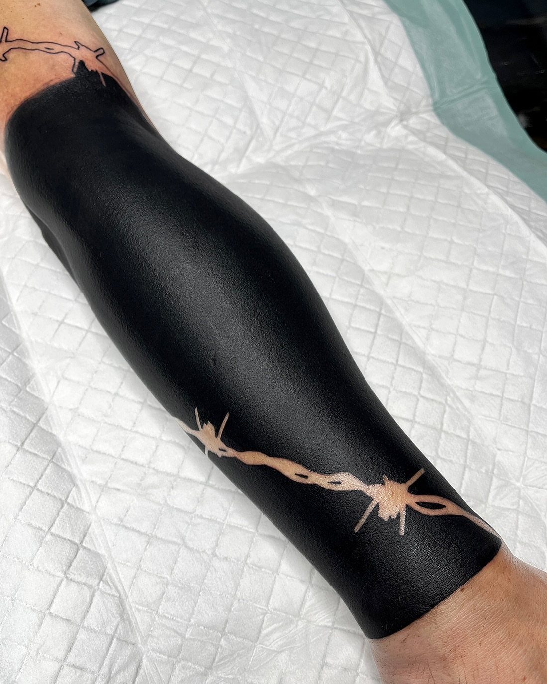 Blackout sleeve tattoo on a forearm with negative space barbed wire design