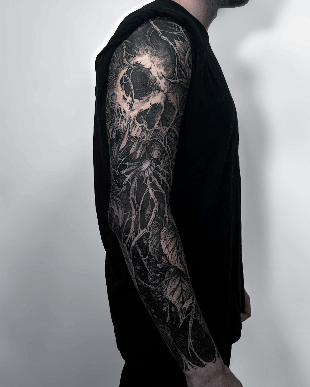 Sleeve tattoo with a skull emerging from a heavy blacked out background.