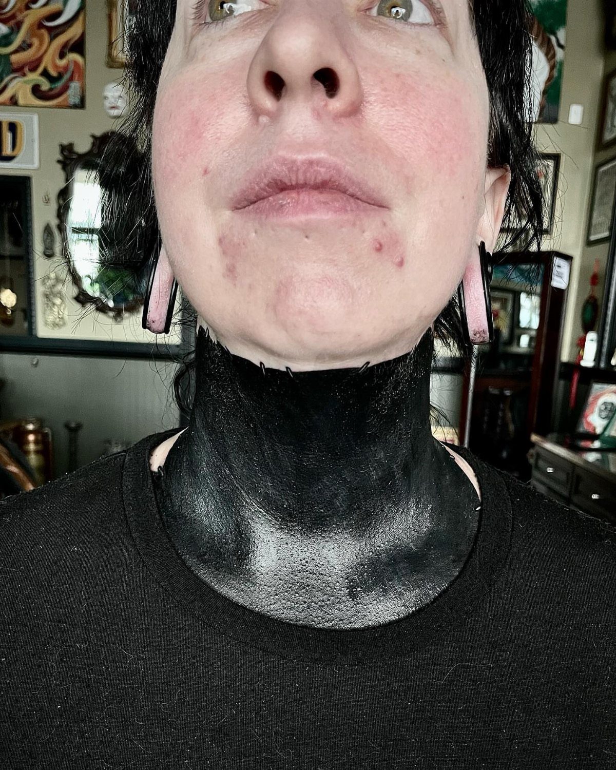 Person with a solid black ink blackout tattoo covering their entire neck.