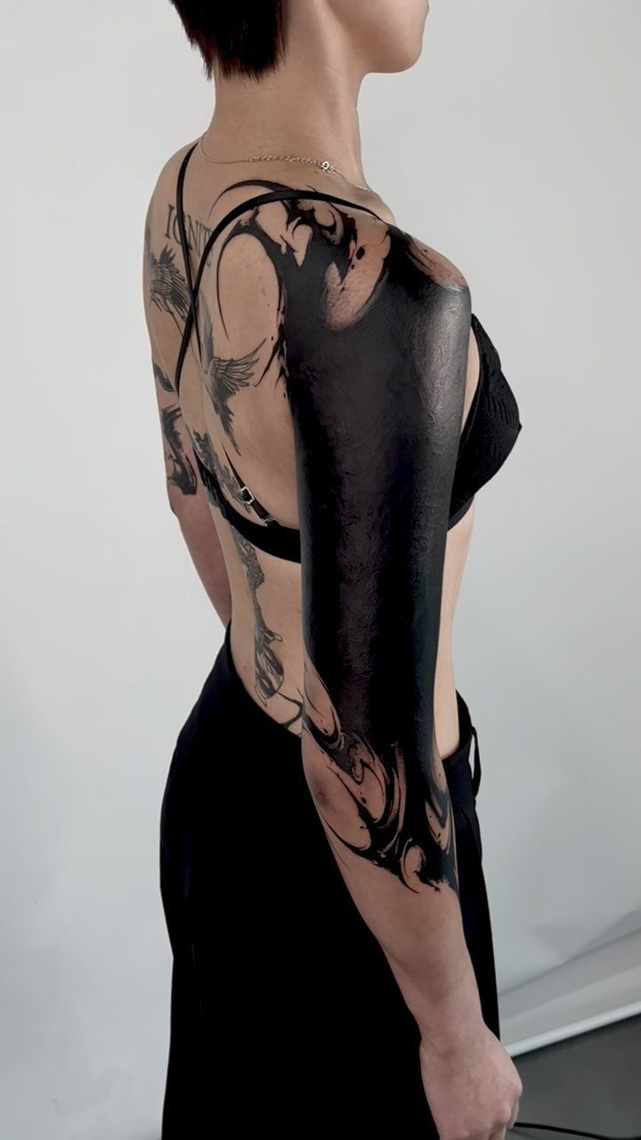 Large solid black ink blackout tattoo covering a person's upper arm and shoulder.