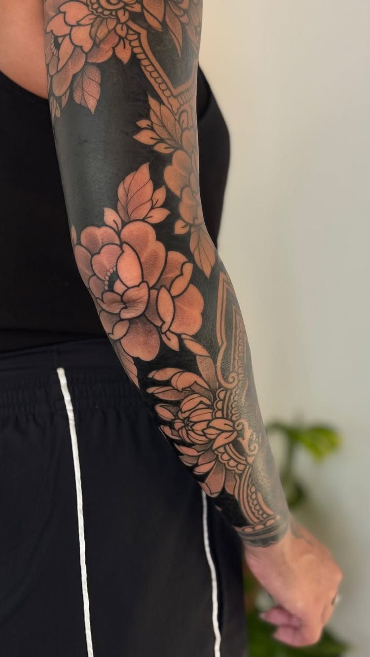 Full sleeve tattoo with large flowers and solid black ink on a person's arm.