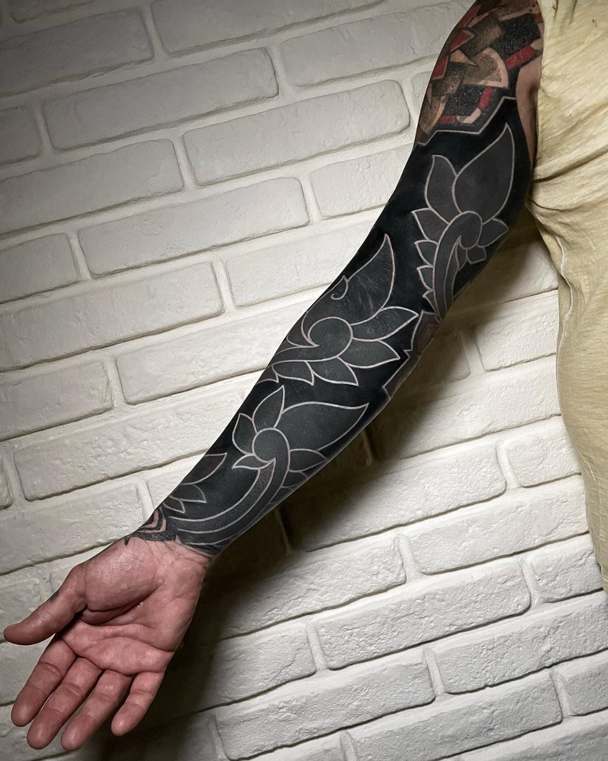 Arm with a blackout cover up tattoo featuring negative space floral designs.