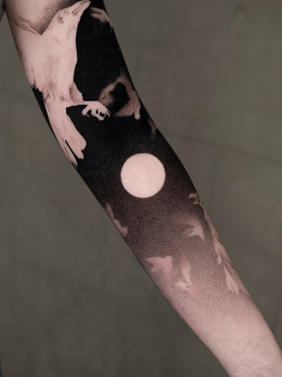 Blackout tattoo on an arm featuring a white raven and a full moon.