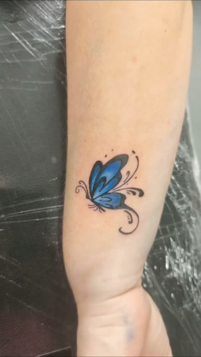 Blue butterfly tattoo with black swirls on a person's forearm.