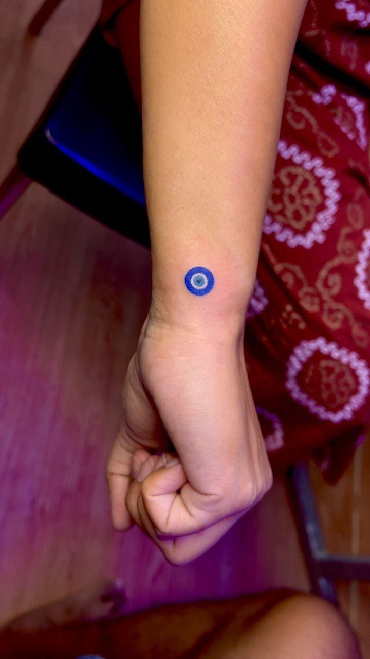 Blue evil eye tattoo on a person's wrist with a dark center pupil.