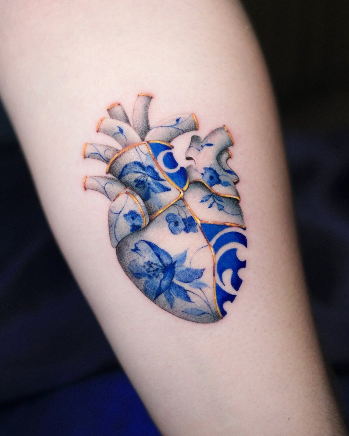 Anatomical heart tattoo with blue porcelain patterns and gold cracks on skin