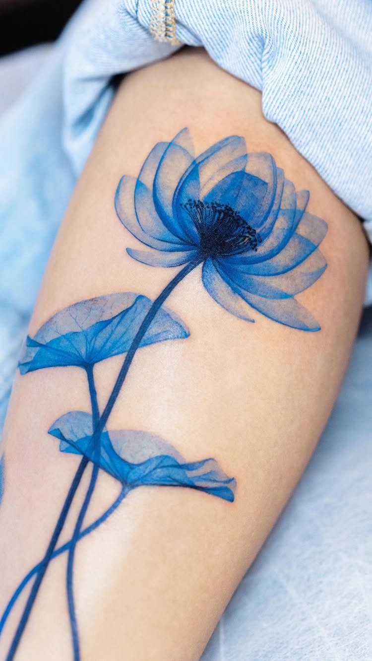 Blue watercolor lotus flower tattoo with leaves on a person's leg