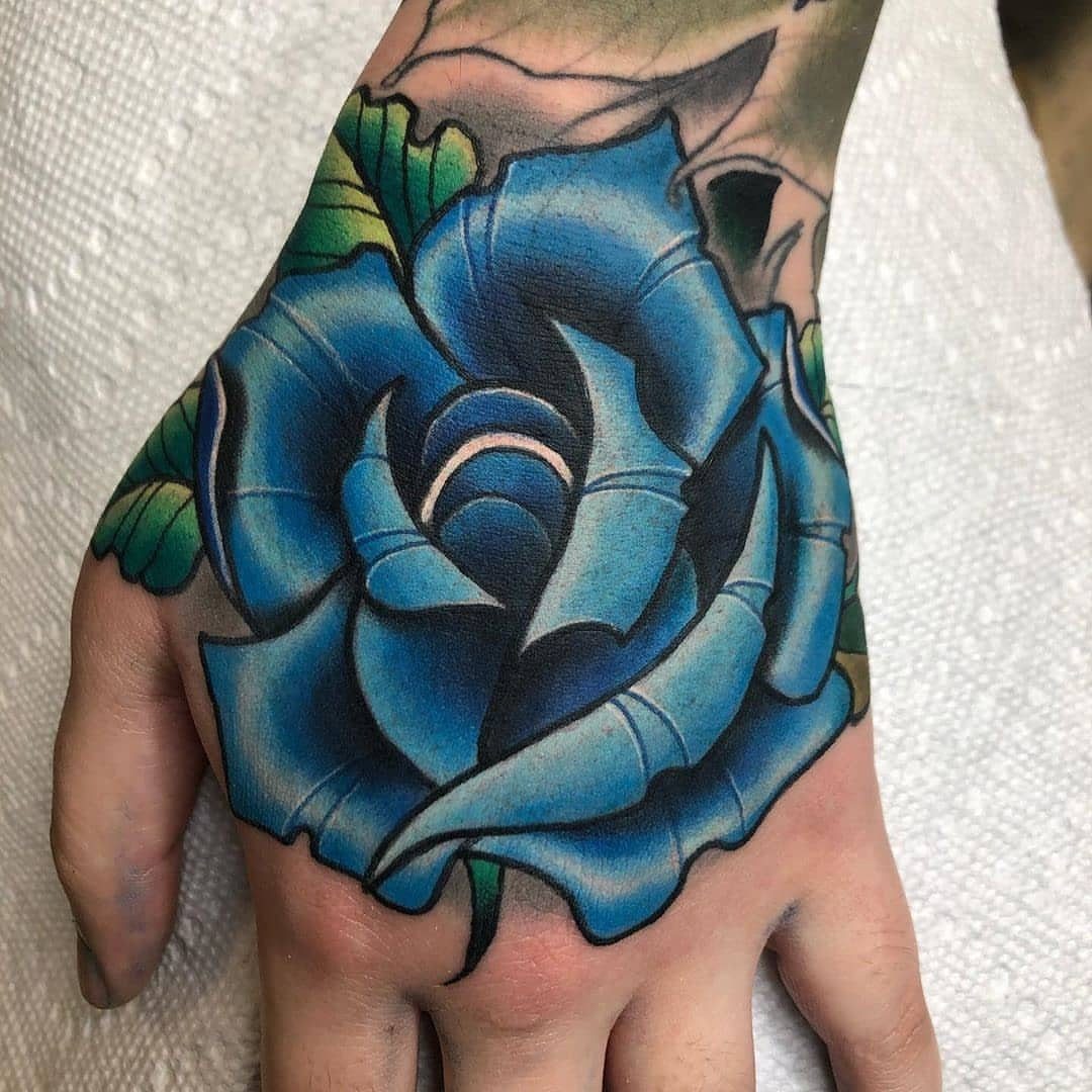 Blue rose tattoo with green leaves covering the back of a person's hand.