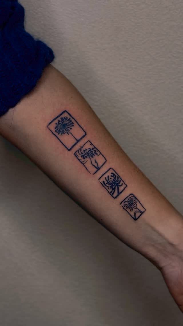 Four small square blue ink tattoos of minimalist flowers on a person's forearm.