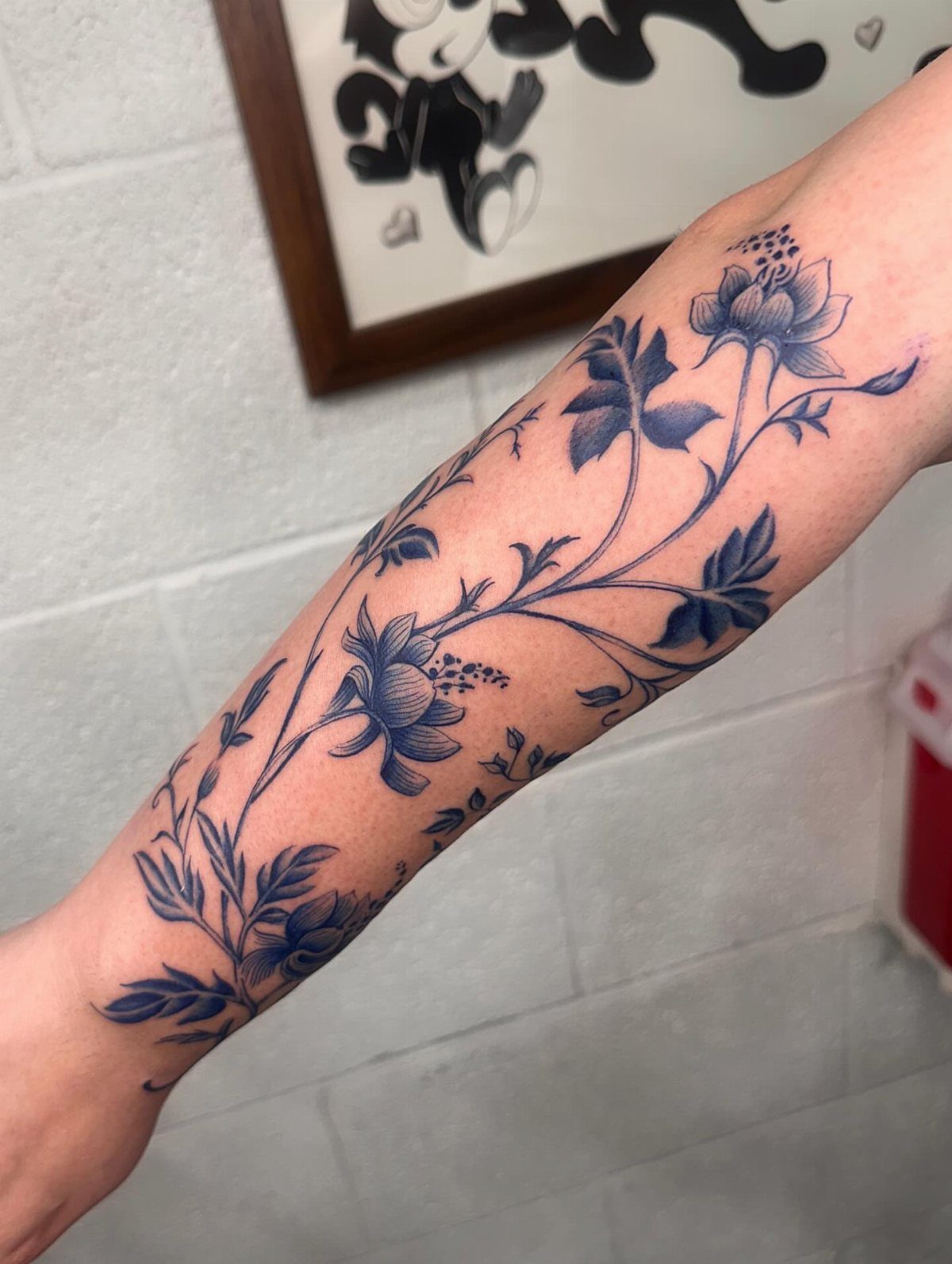 Blue ink floral tattoo of vines and blossoms on a person's forearm.