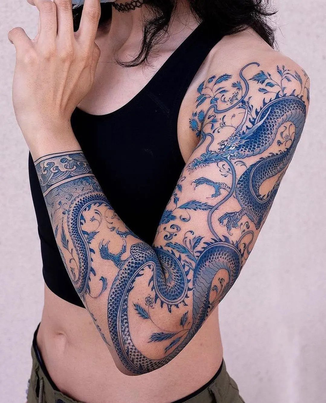 Blue ink dragon tattoo with floral details covering a person's entire arm