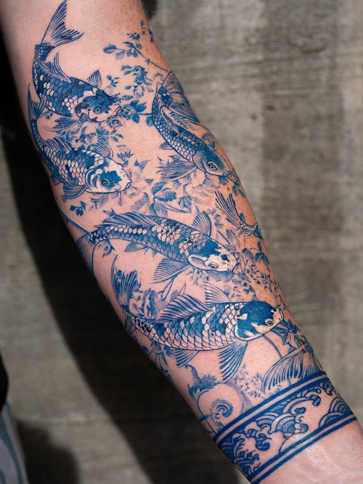 Blue ink tattoo of koi fish and waves on a person's arm