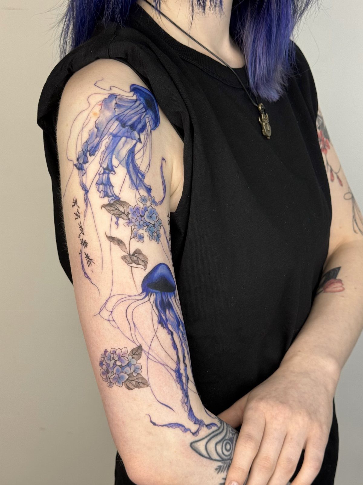 Blue ink tattoo of jellyfish and flowers on a person's upper arm